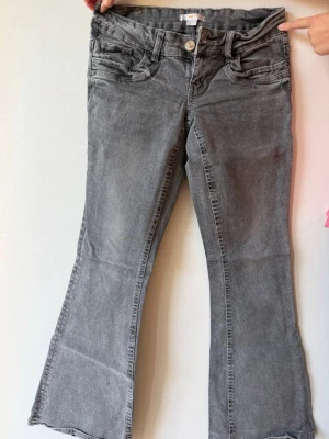 Grå bootcut jeans från Gina Tricot - Snygga grå bootcut jeans från Gina Tricot med klassisk femficksmodell och knappgylf. Jeansen har en lätt utsvängd passform nedtill och är tillverkade i mjukt denimtyg. Perfekta för en trendig och avslappnad look.