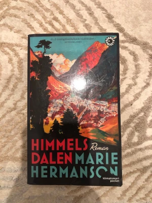 Himmelsdalen av Marie Hermanson - En spännande pocketbok med färgstarkt omslag som visar en dal omgiven av berg. Boken är skriven av Marie Hermanson och är en roman som utspelar sig i Schweiz. Perfekt för dig som gillar thrillers och samhällskritiska berättelser.