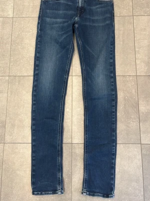 Mörkblå raka jeans - Säljer ett par mörkblå jeans med raka ben och diskret slitning framtill. Jeansen har klassisk femficksmodell och kontrastsömmar. Perfekta till vardags för en avslappnad men snygg look. Vid frågor eller funderingar är de bara att höra av sig!
