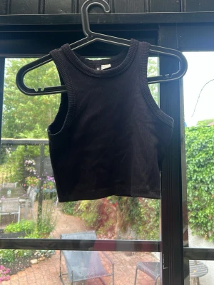 Svart ribbad croppad linnetopp H&M - Säljer en svart croppad linnetopp från H&M Divided. Toppen är ribbad och ärmlös med rund halsringning, perfekt för en chill och trendig look. Passar dig som gillar enkla men snygga basplagg.