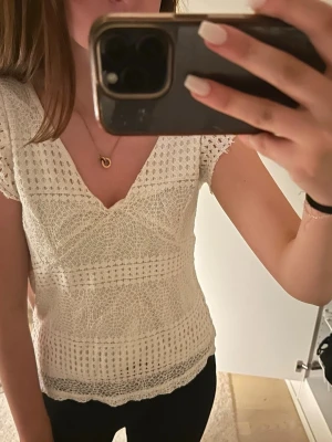 Vit spetsblus med v-ringning - Säljer en söt vit blus med v-ringning och korta ärmar. Blusen har fina spetsdetaljer. Perfekt att styla med jeans eller kjol för en trendig look.