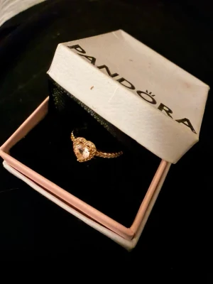 Pandora ring med hjärtformad sten - Söt ring från Pandora i roséguld med en hjärtformad rosa sten i mitten och små gnistrande stenar längs bandet. Kommer i original ask. Perfekt för dig som gillar romantiska och eleganta smycken.