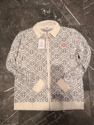 Vit och grå stickad kofta Casablanca - Vit och grå stickad kofta Casablanca. Ny ziptröja i storlek L med prislappar kvar. Mjuk kvalitet med snyggt mönster och broderad logga på bröstet. Modellen är ganska lång och kan sitta som en XL om du vill ha en lite oversized passform.