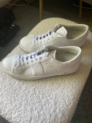 Vita Philippe Model sneakers i skinn - Snygga vita sneakers från Philippe Model Paris i stilren design. Originallåda medkommer. Endast använda enstaka gång, köpta från MerchSweden. Storlek 43.                                                                      köpta för 2999 kr o minimalt använda.