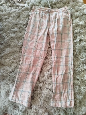 Rutiga rosa pyjamasbyxor - Mysiga pyjamasbyxor i ljusrosa med rutigt mönster i vitt och blått. Byxorna har resår i midjan och snörning för extra komfort. Tillverkade i mjukt tyg som passar perfekt för slappa dagar hemma.