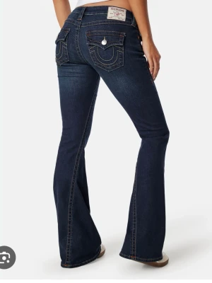Mörkblå bootcut jeans med fickdetaljer - Snygga mörkblå bootcut jeans med kontrastsömmar och dekorativa ficklock bak. Jeansen har en klassisk femficksmodell och utsvängda ben. Materialet är denim med stretch för skön passform. Perfekta för dig som gillar en retroinspirerad look.