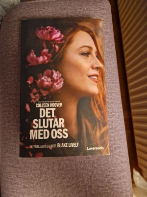 Det slutar med oss av Colleen Hoover - En gripande roman av Colleen Hoover, 'Det slutar med oss', i pocketformat från Lovereads. Omslaget har en bild på en kvinna med blommor i rosa toner och tydlig titeltext. Perfekt för dig som gillar starka berättelser om kärlek och livsval.