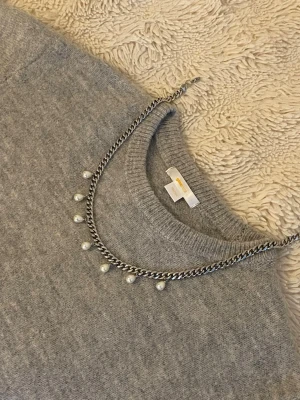 Silverfärgat halsband med pärlor - Snyggt halsband i silverfärgad rostfritt med kedja och sju hängande vita pärlor. Perfekt för att ge en cool touch till din outfit. Stilren design som passar till många olika looks.