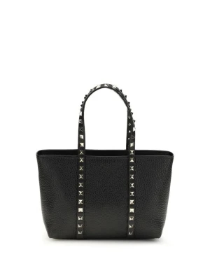 Garavani Rockstud väska  - Den lilla Rockstud Tote Bag från Valentino Garavani är tillverkad av granatatrått kalvskinn och prydd med ikoniska Rockstud-nitar i platin finish. Dess mångsidiga design gör att den kan bäras i handen, över axeln eller crossbody tack vare läderhandtagen och den avtagbara, justerbara remmen. Väskan kompletteras med en dragkedja, skyddande fötter i basen och ett innerfoder, vilket gör den till en elegant och funktionell accessoar för alla tillfällen.
