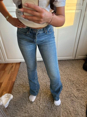 Blå bootcut jeans med hög midja - Säljer ett par ljusblå bootcut jeans med hög midja och klassisk femficksdesign. Jeansen har raka ben som går ut lite nedtill och stängs med knapp och dragkedja. Perfekta till en avslappnad och trendig look.