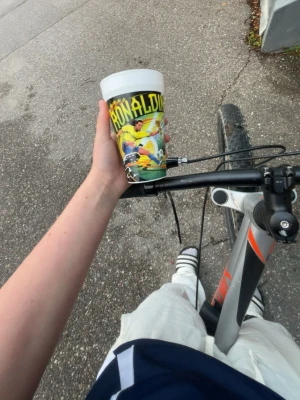 Två plastmuggar med fotbollstryck FIFA world cup - Säljer två färgglada plastmuggar med motiv av kända fotbollsspelare och text. Ena muggen har Ronaldinho-tryck i gult och grönt, den andra har ett motiv av en spelare Beckham som firar mål i blått och rött. Perfekta för sportfans eller som samlarprylar.