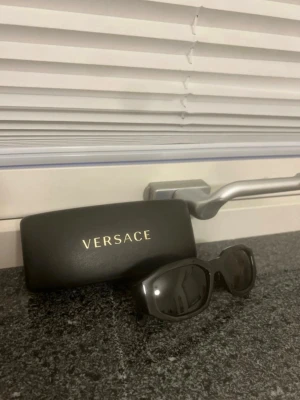 Svarta solglasögon från Versace - Snygga svarta solglasögon från Versace med rektangulär form och ikoniska Medusa-detaljer på skalmarna. Kommer med originaletui. Perfekta för dig som vill ha en stilren och exklusiv accessoar till sommaren. Använda några få gånger. Köpa för 2 800kr men säljs för 1 600kr. Pris går att diskutera. Paketet skickas iväg direkt efter köp för snabb leverans! 🌸