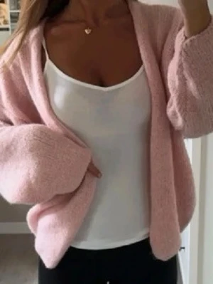 Lindex Ljusrosa fluffig kofta - Mysig ljusrosa kofta med oversized passform och breda ärmar. Koftan är stickad i ett fluffigt material och har en djup V-ringning utan knappar. Perfekt att slänga över en topp för en avslappnad look.