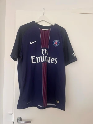PSG matchtröja Verratti Nike - Denna vara är köpt på unisportstore för ett par år sedan. Säljer en mörkblå Paris Saint-Germain matchtröja från Nike med röda och vita detaljer. Tröjan har tryck med 'Verratti' och nummer 6 på ryggen samt klubbmärke och sponsorloggor på framsidan. Perfekt för dig som älskar fotboll och PSG.