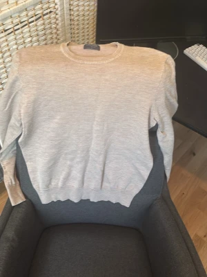 Beige   stickad tröja i bomull - En stilren ljusgrå stickad tröja med rund hals och långa ärmar. Tröjan har ribbade muddar vid ärmslut och nederkant, vilket ger en snygg passform. Perfekt för lager-på-lager och enkel att matcha med olika outfits.