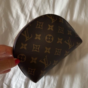 Sminkväska i liten modell monogram necessär - Snygg liten sminkväska el necessär från i klassiskt brunt monogrammönster med guldigt blixtlås. Halvmåneformad modell som är perfekt för smink eller småprylar. Enkel att ta med i väskan och ger en lyxig känsla till vardagen.