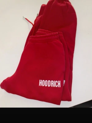Röda mjukisbyxor från Hoodrich - Snygga röda mjukisbyxor från Hoodrich med vit broderad logga på benet. Byxorna har resår i midjan med dragsko och muddar vid bensluten. Tillverkade i mjukt och bekvämt material, perfekta för chill dagar.