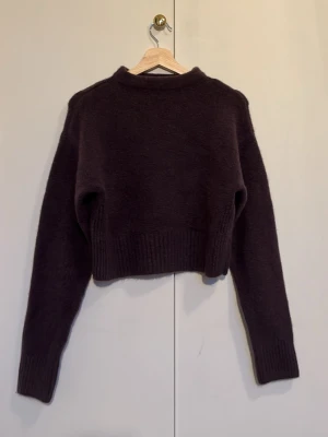 Brun stickad tröja - Säljer en stickad tröja i brun färg. Tröjan har långa ärmar, ribbstickade muddar och en högre rund halsringning. Perfekt för lager på lager och en snygg detalj till din outfit.