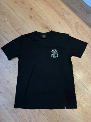 Off-White t-shirt  - Svart t-shirt från Off-White med färgglatt grafiskt tryck på bröstet och klassisk rund hals. Trycket har en fågel och pilar i Off-White-stil. Perfekt för dig som gillar streetwear och vill sticka ut med en unik detalj.