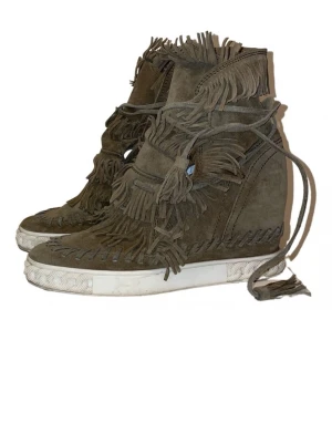 Mörk brons mockasneakers med fransar - Unika höga sneakers från casadei i militär grön mocka med massor av fransdetaljer och snörning. Skorna har en vit sula. Fransarna täcker både fram och sidor. Det är en platå sko så har lite klack. 