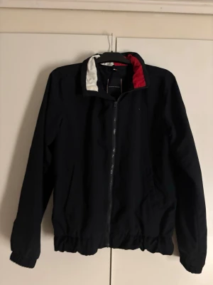 Svart vindjacka från Tommy Hilfiger - Snygg svart vindjacka från Tommy Hilfiger med dragkedja framtill.