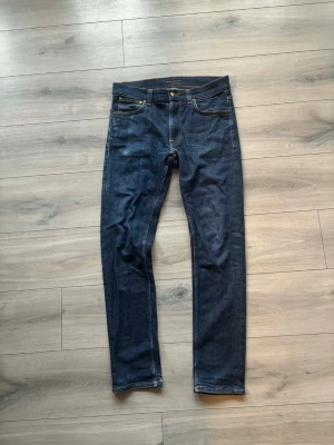Mörkblå jeans från Nudie Jeans - Säljer ett par mörkblå jeans från Nudie Jeans med klassisk femficksmodell och kontrastsömmar. Jeansen har rak passform och är tillverkade i denim med snygg finish. Perfekta för dig som gillar stilrena och tidlösa jeans.