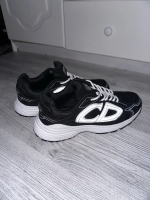 Zara  - Snygga svarta sneakers från Zara med stora vita CD-loggor på sidan och vita snören. Boxen är lite trasig men annars är skorna perfekta!! Pris kan diskuteras!