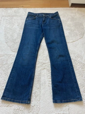 Blå bootcut jeans i klassisk modell - Säljer ett par blå bootcut jeans med normalhög midja och fem fickor. Jeansen har en klassisk tvätt och raka ben som blir vidare nedtill. Tillverkade i slitstark denim med snygga sömmar. Perfekta för en avslappnad och trendig look.