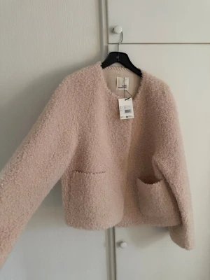 Ljusrosa teddyjacka Sofie Schnoor - Supermjuk teddyjacka i ljusrosa från Sofie Schnoor. Jackan har rund halsringning, två stora fickor framtill och en croppad passform. Tillverkad i fluffigt teddy-material som ger en cozy vibe. Perfekt för dig som vill ha en trendig och bekväm look.