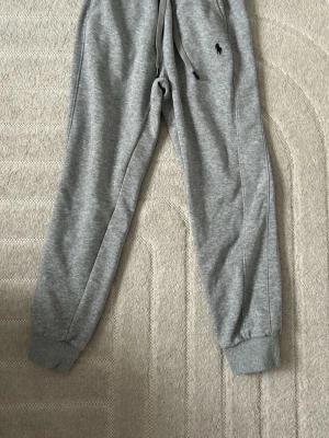 Grå mjukisbyxor från Polo Ralph Lauren - Snygga grå mjukisbyxor från Polo Ralph Lauren med klassisk broderad logga på benet. Byxorna har dragsko i midjan, muddar vid bensluten och är gjorda i mjukt sweatshirtmaterial. Perfekta för chill dagar eller när du vill vara bekväm.