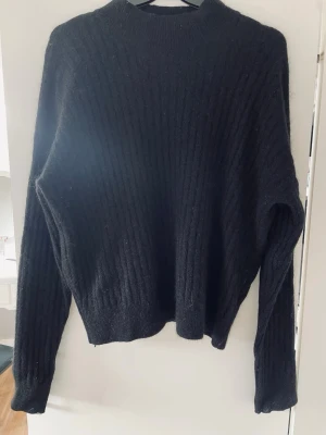 Svart ribbstickad tröja  - Säljer en svart ribbstickad tröja i mohairblandning. Tröjan har lång ärm, hög hals. Från H&M i storlek xs.
