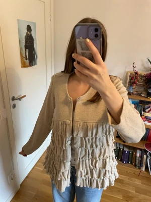 Beige kofta med volangdetaljer - Beige kofta med knappar och flera lager volangdetaljer framtill 