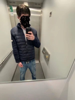 Mörkblå cardiganjacka från Moncler - Snygg mörkblå cardiganjacka från Moncler med quiltad front och stickade ärmar. Jackan har dragkedja framtill, hög krage och Moncler-logga på ärmen. Perfekt för lager-på-lager och streetwear-stil.