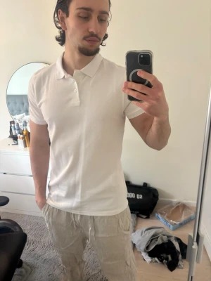 Vit pikétröja i bomull - Klassisk vit pikétröja med krage och knappar framtill. Tillverkad i mjuk bomull och har korta ärmar. Passformen är slim och enkel att matcha med olika stilar.