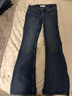 Blå utsvängda jeans från Junkyard - Säljer ett par blå jeans från Junkyard med utsvängda ben och klassisk femficksmodell. Jeansen har snygga kontrastsömmar och coola detaljer på bakfickorna. Perfekta för dig som gillar retrostil och vill sticka ut lite extra. Storlek xs. Använda 1 gång.