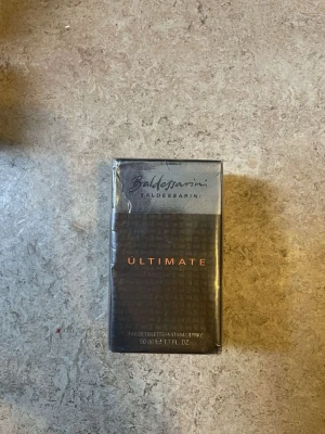 Baldessarini Ultimate Eau de Toilette - Baldessarini Ultimate Eau de Toilette är en parfym för män i en elegant, mörkgrå och silverfärgad förpackning med orange text. Flaskan rymmer 50 ml och har en stilren, maskulin design. Perfekt för dig som gillar exklusiva och moderna dofter.