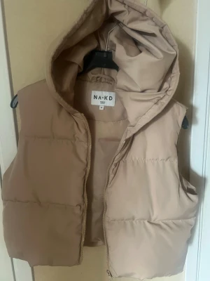 Beige vadderad väst från NA-KD - Snygg beige vadderad väst från NA-KD med dragkedja och stor huva. 