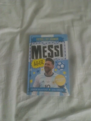 Messi äger - Fotbollsstjärnor - En inspirerande bok om fotbollsikonen Messi från serien Fotbollsstjärnor, skriven av Simon Mugford och Dan Green. Boken har ett blått och vitt omslag med illustrationer, hårdpärm och innehåller roliga fakta, citat och illustrationer om Messis karriär.