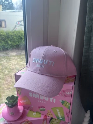 Ljusrosa keps från Smuuti skin - Säljer en ljusrosa keps från Smuutiskin med broderad logga framtill i vitt. Klassisk böjd skärm och justerbar baksida. Perfekt accessoar för en trendig och avslappnad look. Orginal pris: 80kr. Som man kan se på sista bilden är det några sömmar som sticker ut men den kom så. 