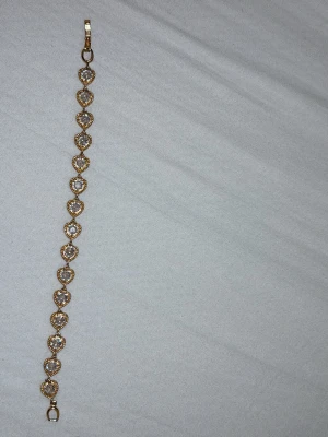 Guldigt armband med hjärtan och pärlor - Snyggt armband i guldfärg med hjärtformade länkar, varje hjärta har en glittrande pärla i mitten. Armbandet har en elegant och romantisk design som verkligen sticker ut. Perfekt accessoar för dig som gillar detaljer och bling.