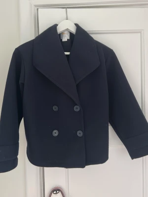 Mörkblå kappa från Gina tricot - Mörkblå kappa ifrån Gina tricot. Kappan har 4 knappar nedtill och är i storleken 146/152. Det finns djur i hemmet så därför kan det finnas nåt hår på kappan men jag försöker såklart få bort så mycket som möjligt. Det finns även knappar längst ut på ärmarna.