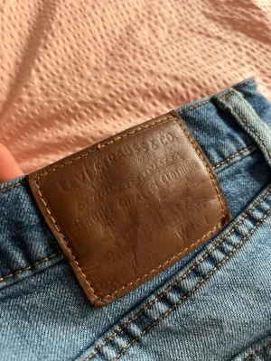 Levi's jeans - Säljer ett par klassiska blå jeans från Levi's med rak passform och snygg slitning framtill. Jeansen har fem fickor, gylf med dragkedja samt den ikoniska bruna läderlappen bak i midjan. Perfekta till en avslappnad stil. Relativt fint skick! Säljes i befintligt skick.