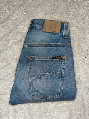 Nudie jeans  - Ljusblåa jeans från Nudie Jeans i modellen Tape Ted. Midja 32cm, längd 105cm. JAG SKICKAR EJ FLER BILDER NÄR JAG BÄR JEANSEN! för bättre inblick i passformen rekommenderar jag att googla på modellnamnet. För storleksguide kolla måtten noggrant då jeansen alltid kan vara uppsydda heller krympta och jag ej tar emot returer :) s6,5