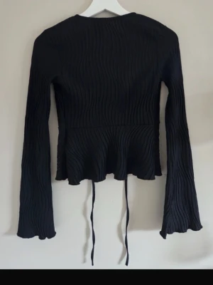 Svart ribbad bolerotopp från gina - Toppen har knytband framtill och en lätt utsvängd nederkant för en snygg siluett. Perfekt att styla över ett linne. Aldrig använd men tyvärr har prislappen lossnat.