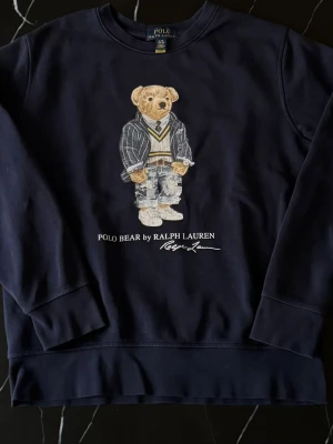 Polo Ralph Lauren Polo Bear Navy Sweatshirt – S/M – Toppskick - Mörkblå Polo Ralph Lauren Polo Bear sweatshirt i väldigt snygg navy färg med klassiska bear-motivet framtill. En riktigt eftertraktad modell som passar perfekt till både casual och clean outfits. Tröjan är i mycket fint skick och sitter snyggt oversized beroende på hur man vill att den ska sitta. Mått: • Längd: 58 cm • Bredd: 50 cm Passar ungefär S/M beroende på önskad fit – kolla måtten för bästa jämförelse. Perfekt till jeans, cargos eller över en skjorta. Svår att hitta i detta skick och färg