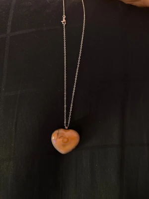 Halsband med hjärt format kristall - Snyggt halsband med ett hjärtformat kristall sten på en tunn silverfärgad kedja. Hjärtat har naturliga mönster och en mjuk glans. Perfekt accessoar för dig som gillar unika smycken med naturlig känsla. Köppt i en lokal kristall shop.