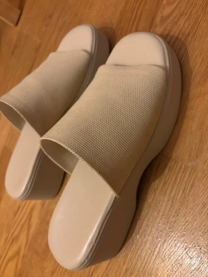 Beige platåsandaler med bred rem - Säljer ett par stilrena beige platåsandaler med bred textilrem och chunky sula. Sandalerna har en minimalistisk design och är perfekta för dig som gillar en clean och modern look. Materialet är en kombination av textil och syntet. Aldrig använda. Storlek 39. 