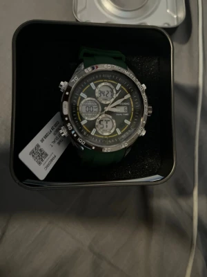 Grön sportklocka från Frederic - Helt ny - Snygg sportklocka från Frederic med grön silikonrem och stor rund urtavla. Behöver pengar inför studenten så säljer billigare då den kostar runt 289 euro på deras sida så jag säljer vidare för 1800 kr men pris kan diskuteras 