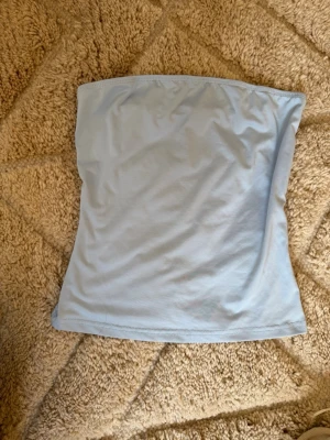 Ljusblå bandeau tubtopp - Säljer en enkel och stilren ljusblå bandeau tubtopp. Toppen är axelbandslös och har en mjuk, stretchig passform som sitter skönt mot kroppen. Perfekt att matcha med jeans eller kjol för en fräsch look.