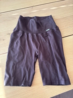 Bruna ribbade cykelshorts - Säljer ett par bruna ribbade cykelshorts med hög midja. Shortsen har en stretchig passform och är tillverkade i ett mjukt material som passar perfekt till träning eller chill. Snyggt ribbat mönster över hela plagget för en modern look. Ifrån Aimn storlek s